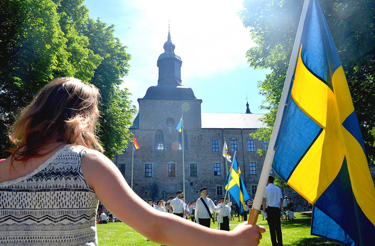 Kvinna som håller svensk flagga med Vadstena slott i bakgrunden