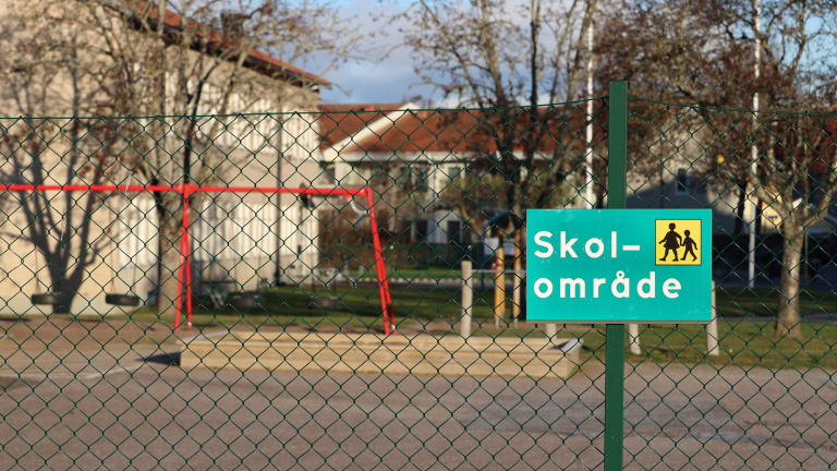 Skylt med texten "skolområde" med skolgård bakom.