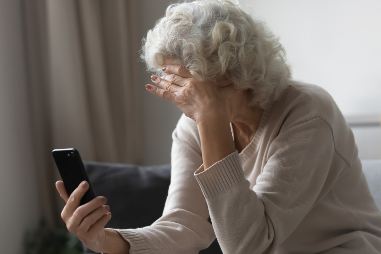 Sorgsen äldre kvinna med mobiltelefon i handen